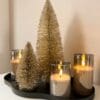 Champagne kleurige decoratie kerstboompjes in twee verschillende hoogtes, gedecoreerd op een plateau met 3 ledkaarsen in een glas erbij