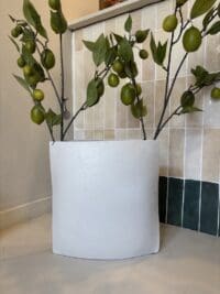 Platte metalen vaas in off white met ruwe afwerking van 37 cm op de vensterbank